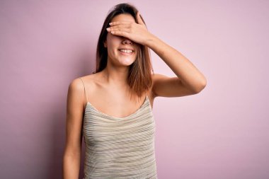 Genç, güzel esmer kız, pembe arka plan üzerinde sıradan çizgili tişört giyiyor. Gülümsüyor ve yüzünde şaşkınlık için gözleri kapayarak gülüyor. Kör kavram.