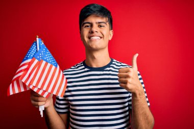 Amerika Birleşik Devletleri bayraklarını tutan genç yakışıklı vatansever adam büyük bir gülümsemeyle bayrak sallıyor.