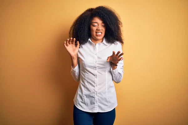 Young beautiful african american elegant woman with afro hair standing over yellow background disgusted expression, displeased and fearful doing disgust face because aversion reaction.