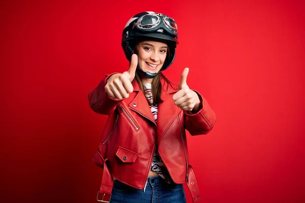 若い美しいブルネットのオートバイのヘルメットと赤いジャケットを身に着けているオートバイの女性は 手で肯定的なジェスチャーを行うことを承認し 親指を上げて笑顔と成功のために幸せ 勝者のジェスチャー — ストック写真