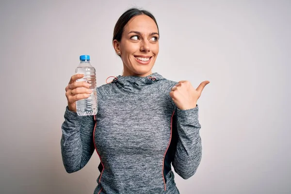 年轻的健身女子穿着运动服 从塑料瓶里喝水 用手指和大拇指朝外看 面带微笑地笑了笑 — 图库照片