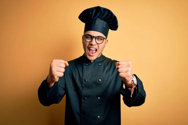 年轻的巴西厨师 身穿炊事服 头戴帽子 头戴孤立的黄色背景 怒气冲冲地举起拳头 怒气冲冲地大喊 愤怒和好斗的概念 — 图库照片