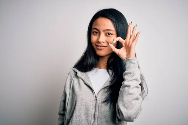 隔離された白い背景の上にスウェットシャツを身に着けている若い美しい中国のスポーティな女性は手と指でOkサインをして肯定的な笑顔 成功した表現 — ストック写真