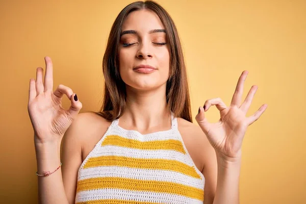 年轻美丽的黑发女子 穿着浅黄背景的休闲条纹T恤 闭上双眼微笑 用手指做冥想动作 瑜伽概念 — 图库照片