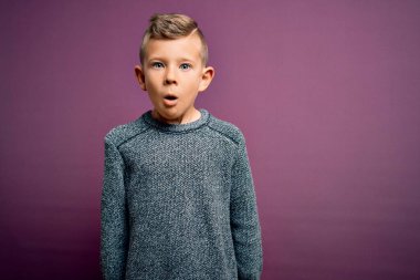 Mavi gözlü küçük beyaz çocuk mor arka planda dikilmiş korku, korku ve heyecan dolu yüz ifadesiyle şok olmuş ve korkmuştu..