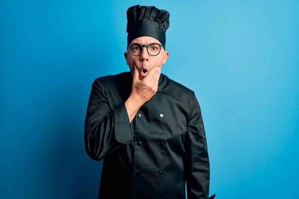 Middle age handsome grey-haired chef man wearing cooker uniform and hat Looking fascinated with disbelief, surprise and amazed expression with hands on chin