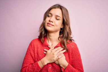 Pembe izole edilmiş arka planda, elleri göğsünde, gözleri kapalı ve yüzünde minnet dolu hareketlerle gülümseyen genç, güzel sarışın bir kız. Sağlık kavramı.