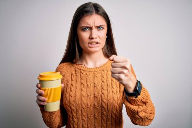 Mavi gözlü genç bir kadın izole edilmiş arka planda bir fincan kahve içiyor sinirlenmiş ve sinirlenmiş bir şekilde bağırıyor, çıldırmış ve el kaldırarak bağırıyor. Öfke kavramı.