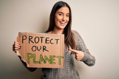 Genç ve güzel esmer kadın gezegenimizi korumak için protesto yapıyor. Posteri tutarken mutlu bir şekilde eliyle ve parmağıyla işaret ediyor.