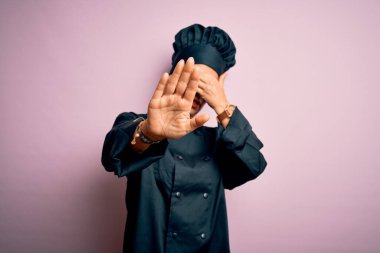 Orta yaşlı esmer aşçı kadın aşçı üniforması giyiyor ve pembe arka plan üzerine şapka takıyor gözleri ellerle örtüyor ve üzgün ve korku ifadeleriyle jest yapıyor. Utanç verici ve olumsuz bir kavram..