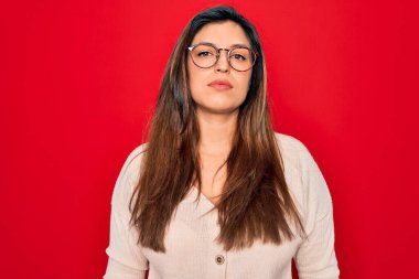 Kırmızı izole edilmiş arka planda duran gözlüklü, İspanyol asıllı, zeki bir kadın yüzünde ciddi bir ifadeyle rahatlamış. Basit ve doğal bir şekilde kameraya bakıyorsun..
