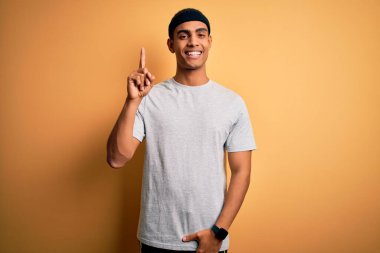 Sarı arka plan üzerine spor giyerek spor giyinen yakışıklı Afro-Amerikan sporcusu başarılı bir fikri işaret ediyor. Heyecanlı ve mutlu. Bir numara..