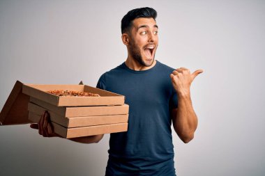 Beyaz arka planda İtalyan pizzası olan teslimat kutuları taşıyan yakışıklı bir adam başparmağıyla gülümseyen bir gülümseme gösteriyordu.