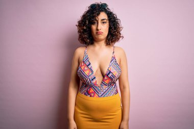 Genç, güzel bir Arap kadın, pembe arka planda mayo ve güneş gözlüğü takarak tatilde. Depresyona girmiş, üzüntüden ağlayan, sinirli ve korkmuş. Üzücü ifade.