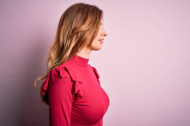 Genç, güzel, esmer bir kadın pembe arka plan üzerinde sıradan bir süveter giyiyor, yan yana bakıyor, rahat bir görünüm sergiliyor kendine güvenen bir gülümsemeyle doğal bir yüz ifadesi sergiliyor..