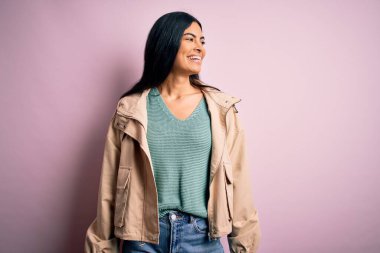 Kış ceketi ve pembe arka planda süveter giyen, yüzünde gülümseme ve doğal bir ifadeyle yan yana bakan genç, güzel İspanyol moda kadını. Kendinden emin gülen.