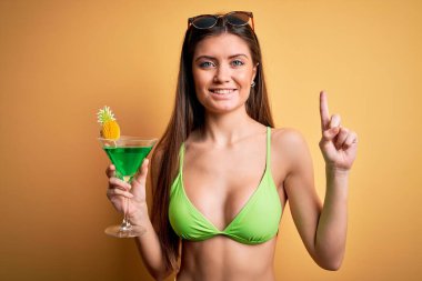 Tatilde mavi gözlü, bikini giyen, kokteyl içen genç, güzel bir kadın bir fikir veya soru işareti ile şaşırmış, mutlu yüzlü, bir numara.