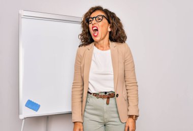 Orta yaşlı bir iş kadını, kızgın ve kızgın bağıran kızgın ve öfkeyle bağıran bir karatahta tarafından sunulan seminer sunumunda duruyor. Öfke ve agresif kavram.