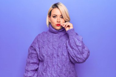 Güzel sarışın ve boyunda bir kadın mor arka plan ağzının üzerine balıkçı yaka kazak giyiyor ve dudakları parmaklarıyla fermuar gibi kapalı. Gizli ve sessiz, tabu konuşması