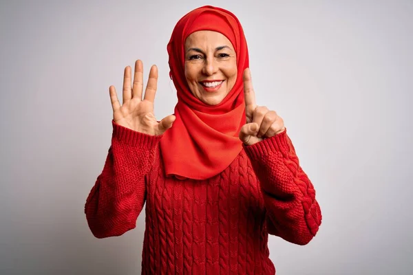 Middle age brunette woman wearing muslim traditional hijab over isolated white background showing and pointing up with fingers number six while smiling confident and happy.