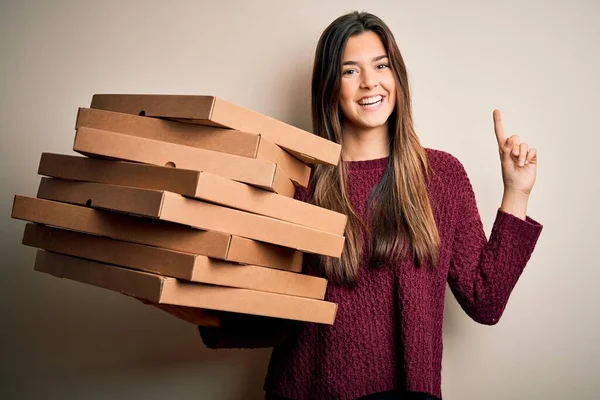 年轻而漂亮的姑娘拿着意大利披萨盒 站在白色的背景上 惊讶地发现了一个主意或问题 她满脸喜形于色 指手画脚 排在第一位 — 图库照片