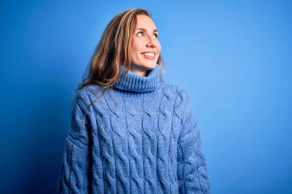 若い美しいブロンドの女性の顔に笑顔で横に離れて見て青の背景にカジュアルなタートルネックセーターを着て 自然な表情 自信を持って — ストック写真