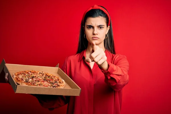 年轻美丽的黑发女子拿着装有意大利披萨的送货盒 红色背景 手指指向摄像机和你 正面是积极自信的手势 — 图库照片