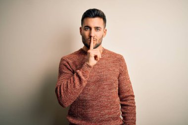 İzole edilmiş beyaz arka planda sıradan bir süveter giyen genç ve yakışıklı bir adam sessiz olmak istiyor. Sessizlik ve gizli konsept.