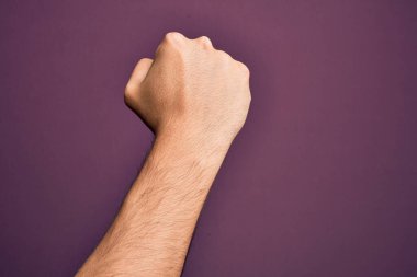 İzole edilmiş mor arka planda parmaklarını gösteren beyaz bir genç adam protesto ve devrim hareketi yapıyor, güç ve güç gösterisi yapıyor.