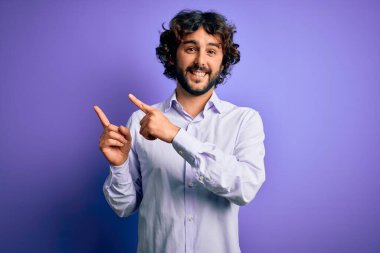 Mor arka plan üzerinde duran sakallı yakışıklı iş adamı gülümsüyor ve kameraya bakıyor iki eliyle ve parmaklarıyla kenarı işaret ediyor..