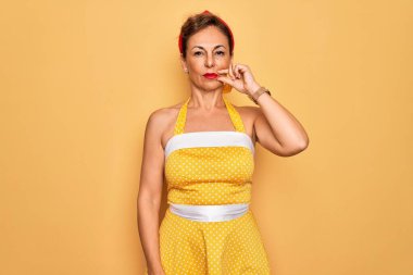 Orta yaşlı bir kadın, 50 'li yaşların modasına uygun bir elbise giymiş sarı arka plan ağzı ve dudakları parmaklarıyla kapanmış bir fermuar gibi. Gizli ve sessiz, tabu konuşması
