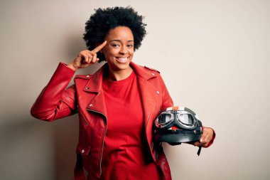 Kıvırcık saçlı motosiklet kasklı genç Afrikalı Afrikalı motosikletçi kadın. Tek parmağıyla kafasını gösteren gülümsüyor. Harika bir fikir ya da düşünce.