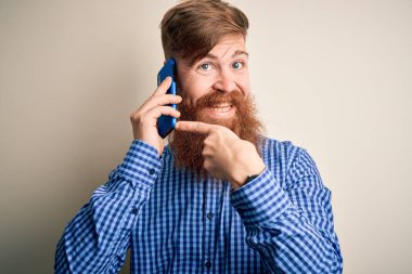 Kızıl saçlı, sakallı, akıllı telefondan konuşan, izole edilmiş arka planda yaşayan bir İrlandalı. Elle ve parmakla göstererek çok mutlu.