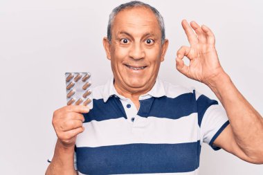 Gri saçlı yaşlı adam hapları tutuyor. Parmaklarıyla imza atıyor. Gülümsüyor. 