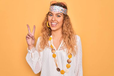 Mavi gözlü, güneş gözlüklü ve aksesuarlı güzel sarışın kadın kameraya bakıp zafer işareti yapıyor. İki numara..