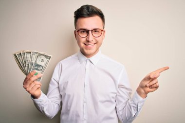 Beyaz saçlı yakışıklı bir iş adamı, elinde bir sürü banknotla mutlu bir şekilde elini ve parmağını kenarı işaret ediyor.