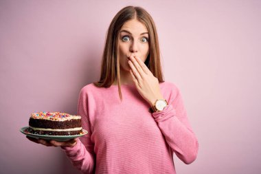 Genç, güzel kızıl saçlı bir kadın, pembe arka plan örtüsünün üzerinde doğum günü pastası tutuyor. Ağzı kapalı, utancından ağzı açık, korkusunun dışa vurumu, sessizlikten korkması, gizli konsept.