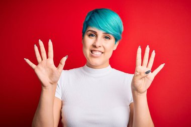 Mavi saçlı, kırmızı arka planda sıradan tişörtler giyen genç ve güzel bir kadın dokuz numarayı gösterirken kendine güvenen ve mutlu bir şekilde gülümsüyor..