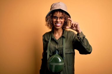 Genç Afro-Amerikan turist kadın tatilde. Kaşif şapkası ve su kantini takıyor. Gülümsüyor ve el hareketleriyle el hareketi yapıyor. Ölçü kavramı.