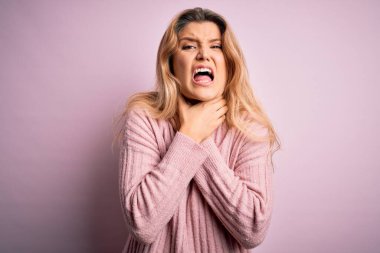 Genç, güzel, sarışın bir kadın izole edilmiş arka planda pembe süveter giyiyor bağırıyor ve boğuluyor çünkü acı verici bir boğulma var. Sağlık problemi. Boğulma ve intihar konsepti.