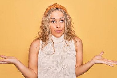 Sarışın, sıradan tişörtler giyen güzel bir kadın ve izole edilmiş sarı arka plan, bilgisiz ve elleri havada, kafası karışmış bir ifade. Şüphe kavramı.