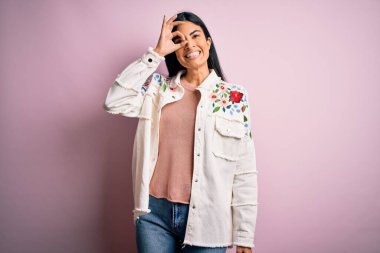 Pembe arka planda günlük süveter giyen genç, güzel İspanyol moda kadını el hareketleriyle gülümsüyor ve mutlu yüzüyle parmaklarının arasından bakıyor..