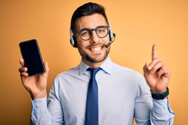 Çağrı merkezinden gelen müşteri hizmetleri kulaklığı olan bir işletmeci bir fikir ya da soru işareti ile şaşırmış bir numara olan mutlu yüzlü akıllı telefon ekranını gösteriyor.