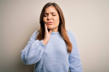 Kış süveteri giyen genç ve güzel bir kadın izole bir arka planda durup diş ağrısı ya da diş hastalığından dolayı acı dolu bir ifadeyle ağıza dokunuyor. Dişçi