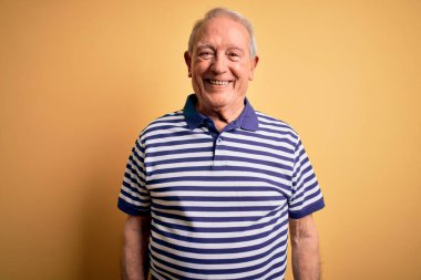 Gri saçlı, donanma çizgili tişört giyen, mutlu ve havalı bir gülümsemeyle sarı arka planda duran son sınıf öğrencisi. Şanslı kişi..