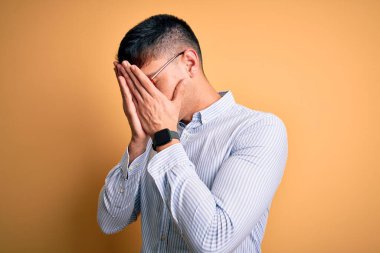 Sarı arka planda inek gözlüğü takan genç, yakışıklı İspanyol iş adamı. Ağlarken yüzünü ellerle kapatan üzgün bir ifade. Depresyon kavramı.