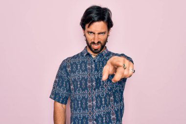 Genç, yakışıklı, bohem, pembe arka plan üzerine hippi tarzı giyinmiş bir adam. Kameraya kızgın ve sinirli olduğunu gösteriyor.