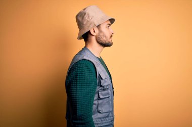 Tatilde sakallı yakışıklı turist sarı arka planda gezen kaşif şapkası takıyor rahat bir görünüm ve kendine güvenen bir gülümseme takınıyor..