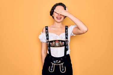 Mavi gözlü genç bir Alman kadın geleneksel Ekim Festivali elbisesi giyiyor. Gülümsüyor ve elleri yüzünde gülüyor. Şaşırtmak için gözleri örtüyor. Kör kavram.