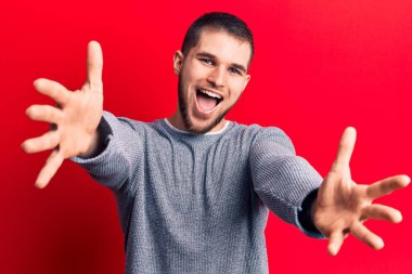 Gündelik kazak giyen genç yakışıklı adam kameraya sarılmak için kollarını açıp gülümsüyor. Mutluluğu kucaklayan neşeli bir ifade.. 